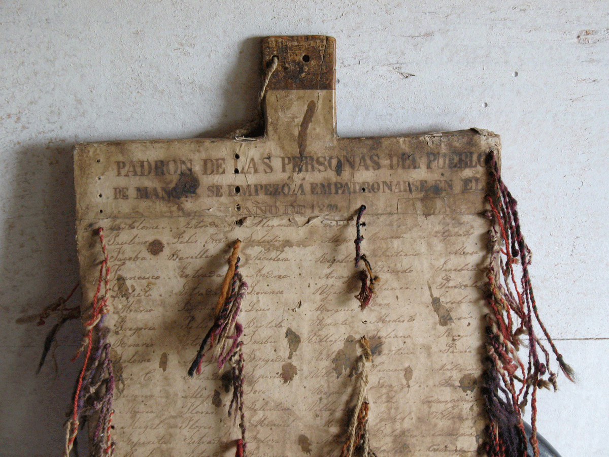 A weathered wooden board from Mangas carries printed headings and handwritten names, with colored cords passing through holes in the board.